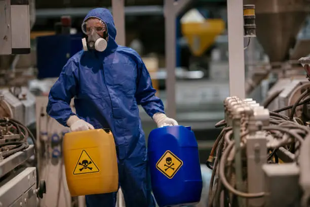 Worker in protective gear handling hazardous waste containers in an industrial setting, highlighting legal obligations related to hazardous materials in Texas probate properties.