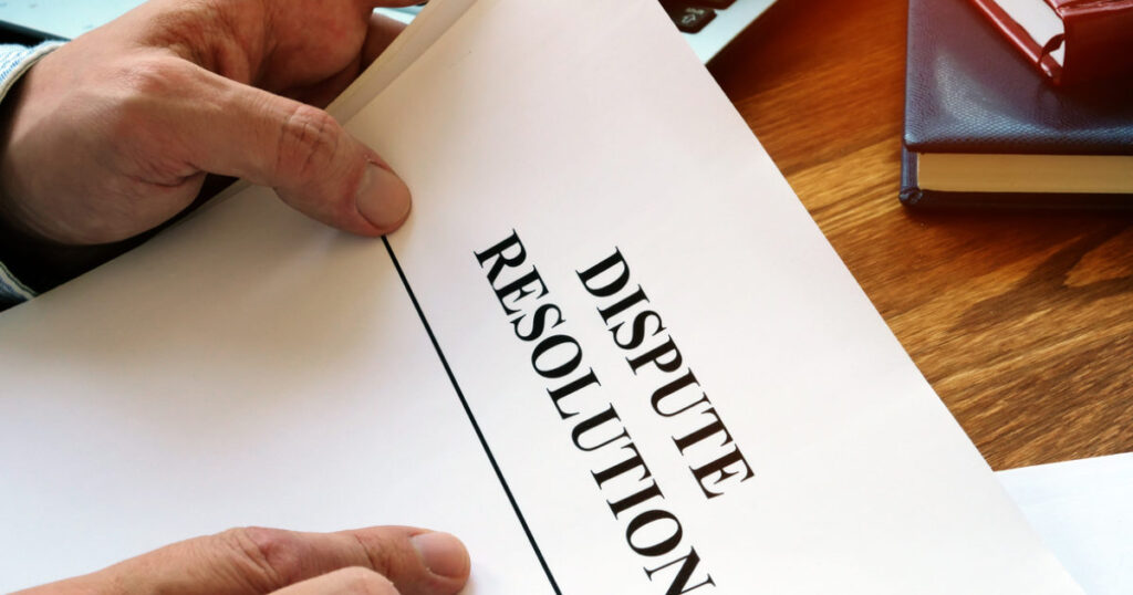 Hands holding a document titled "DISPUTE RESOLUTION" on a wooden desk, symbolizing legal processes in probate disputes and resolutions.