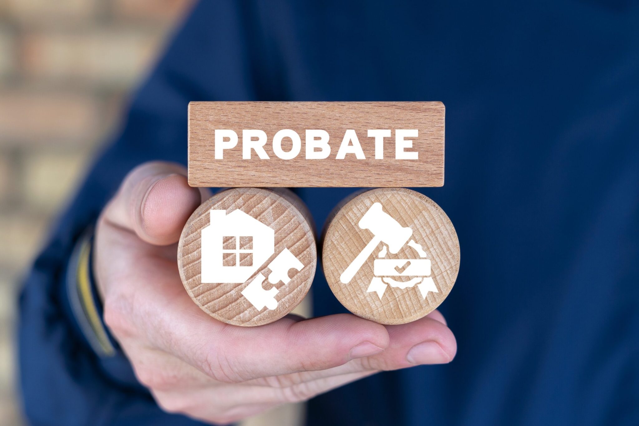 Hand holding wooden blocks labeled "PROBATE," featuring icons of a house and puzzle piece on one block, and a gavel with a certificate on the other, symbolizing estate planning and legal processes related to probate.