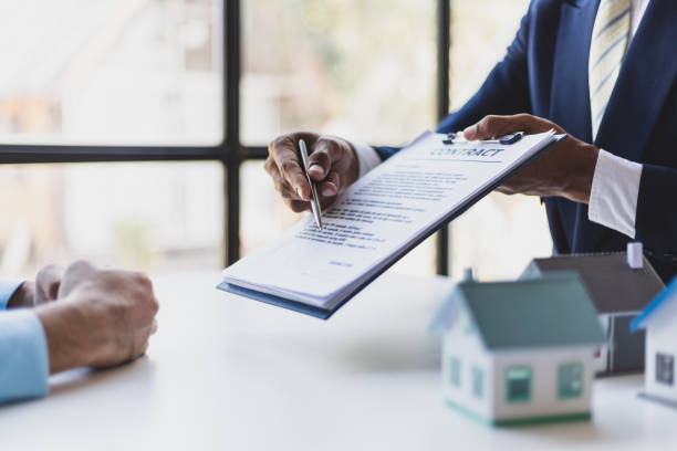Businessman or lawyer pointing at contract agreement document with pen for client to sign, with miniature houses on the table, illustrating legal ownership and property transactions in Texas probate law.