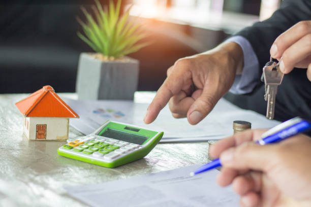 Real estate agent holding house keys and pointing at calculator during contract signing in office setting, symbolizing property transactions related to probate issues in Texas.