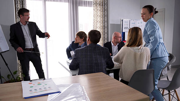 Business meeting with a diverse group of professionals discussing strategies, with one person presenting and others engaged in conversation, emphasizing collaboration and communication in estate planning and dispute resolution.