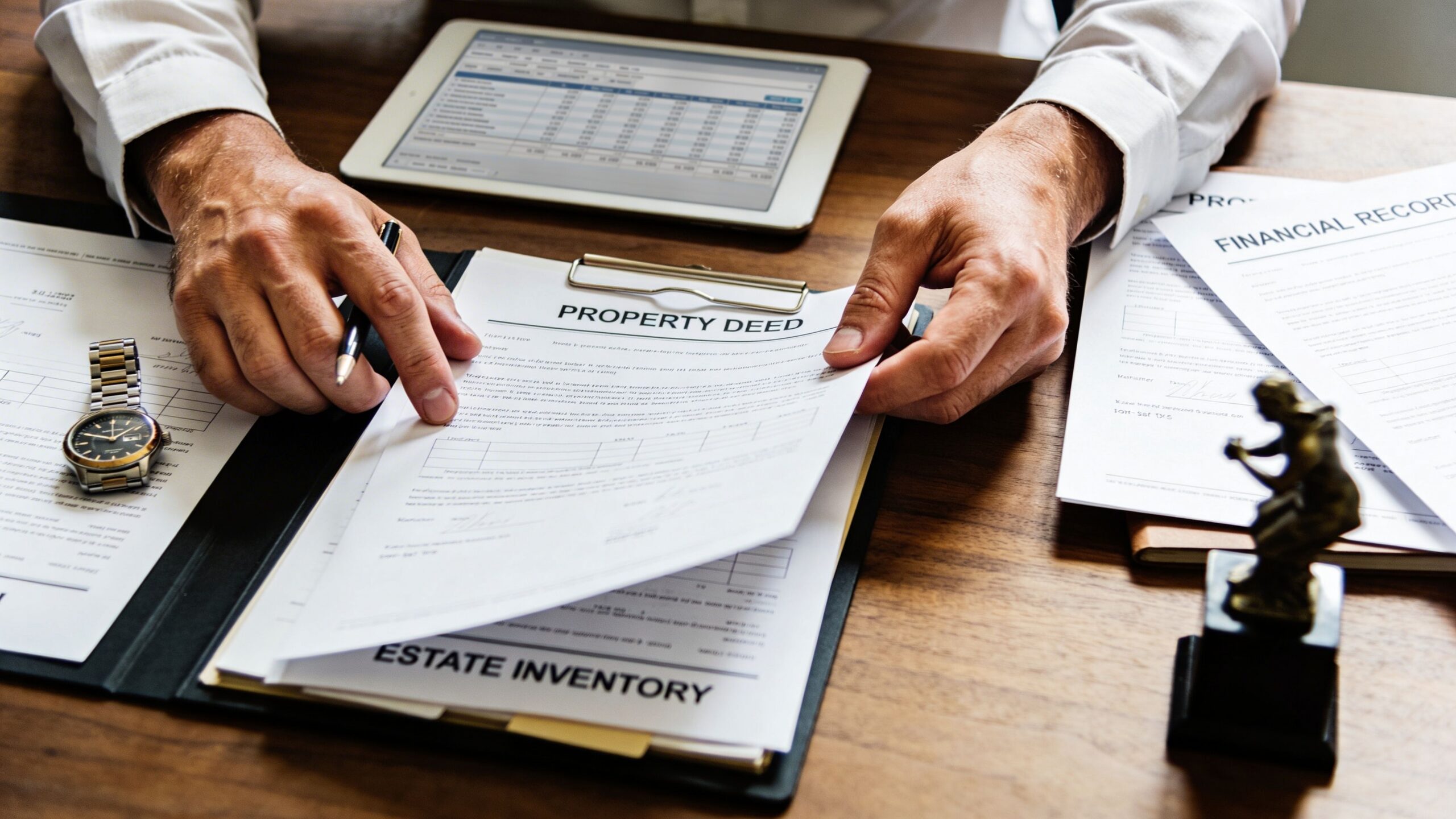 A professional reviewing legal documents including a property deed and estate inventory on an office desk.