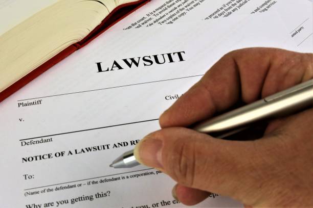 Hand holding a pen above a legal document titled "LAWSUIT," with a blurred book in the background, illustrating the complexities of lawsuits in Texas probate law.