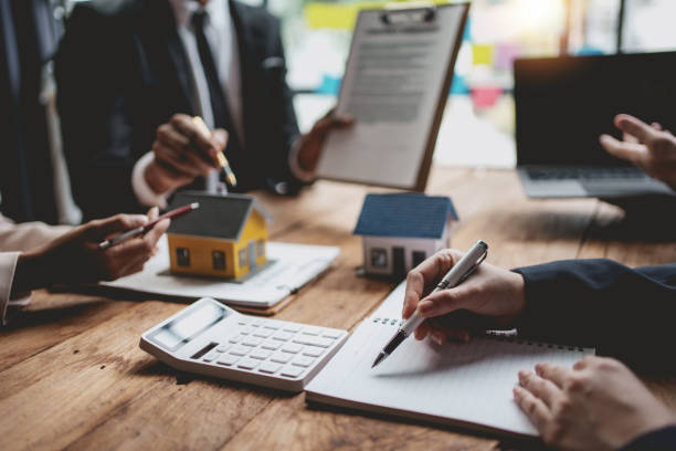 Group of real estate professionals discussing property management strategies, with miniature houses, paperwork, and a calculator on the table, illustrating teamwork in probate law contexts.