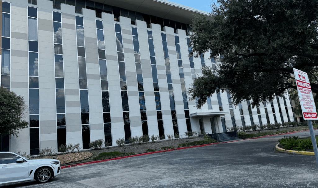 River Oaks office building of the Law Office of Bryan Fagan PLLC, featuring modern architecture with a glass facade, surrounded by greenery and a parking area.