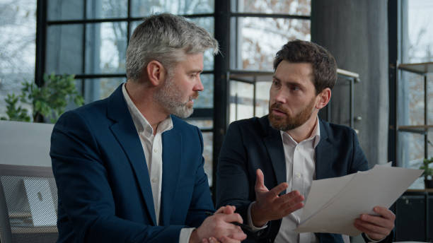 Two frustrated Caucasian businessmen discussing a contract in a modern office setting, reflecting themes of trust mismanagement and fiduciary responsibilities.