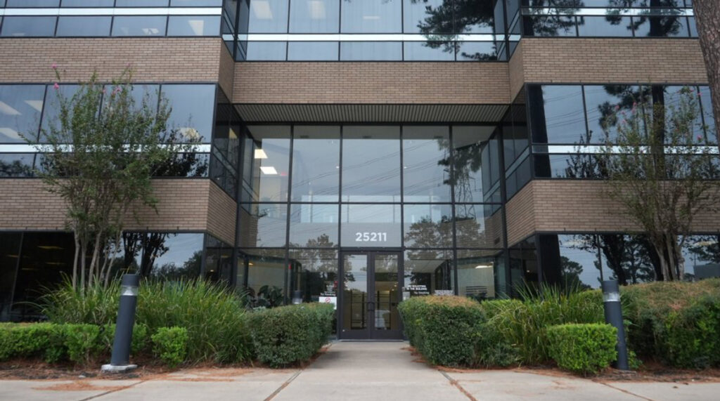 Office building of the Law Office of Bryan Fagan in The Woodlands, Texas, featuring large glass windows, entrance with address 25211, and surrounding greenery.