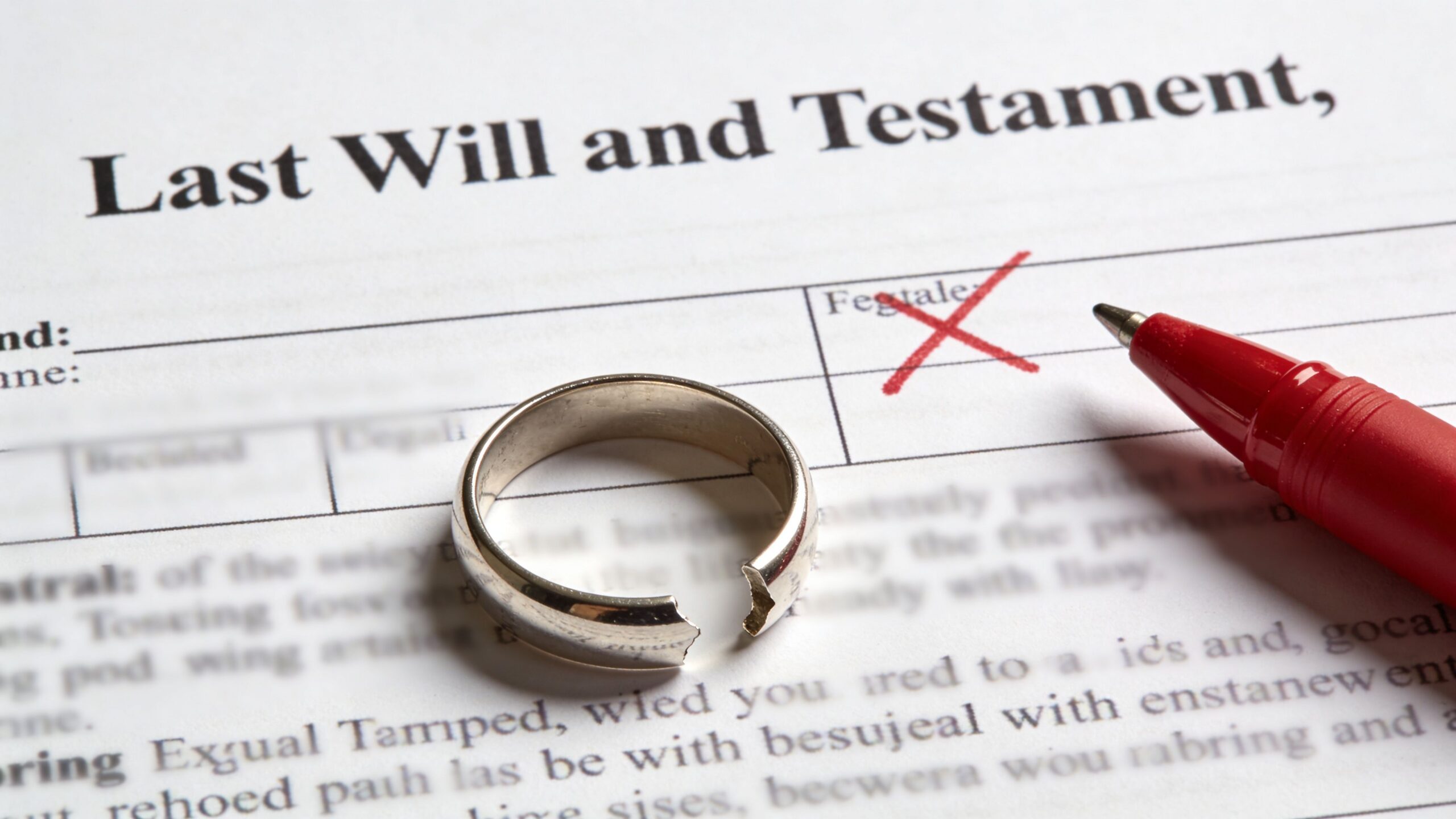 A broken wedding ring sits on a Last Will and Testament document next to a red pen.