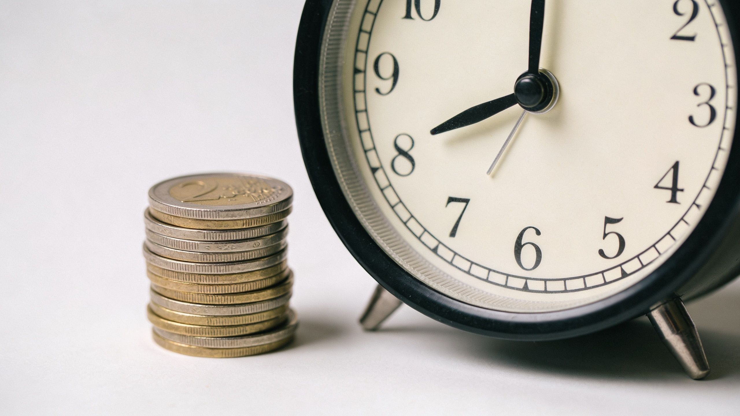 A stack of two euro coins placed beside a black analog clock on a white background.